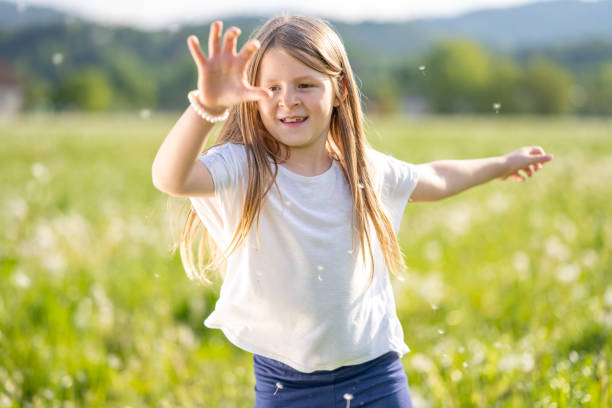 Smiling girl playing with dandelion seeds in meadow during sunny day.