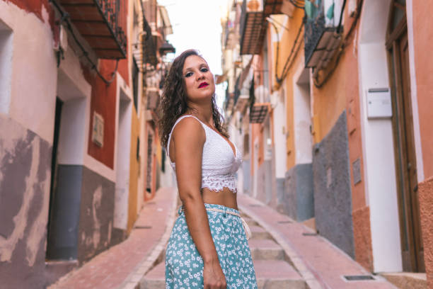 femme brune sérieuse posant dans l’une des rues avec des escaliers dans la ville colorée de villajoyosa, alicante, espagne. - looking off camera photos et images de collection