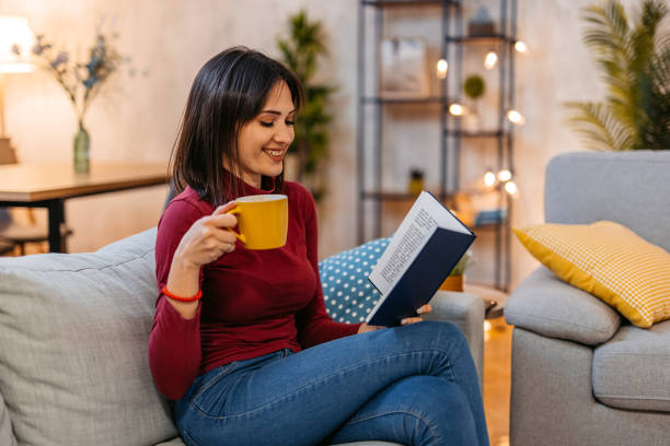 istock Young Woman Reading A Book And Drinking Coffee At Home At Night 1470449287