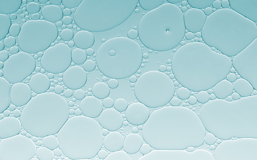 Beautiful and fantastic macro photo of oil and water droplets on surface with pale blue background.