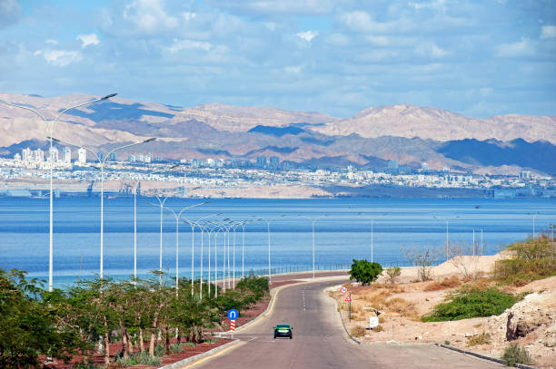 View over coastal road from Aqaba towards Israel and the city of Eilat, Aqaba, Jordan View from Aqaba towards Israel and the city of Eilat, Aqaba, Jordan, Middle East. The close proximity of the disputed lands of Israel, Palestine and Jordan illustrates the ongoing tensions between the nations in terms of sovereignty over the territories - a conflict likely to prevail for many years akaba stock pictures, royalty-free photos & images