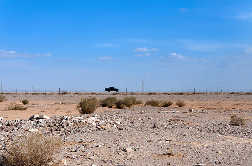 Pickup truck crossing Jordanian Desert, Highway 40, Jordan, Middle East. Vehicles traverse the barren desert landscape of Jordan's Highway 40, roughly 85 kilometers (53 mi) from Amman in the Jordanian Desert, one of the most inhospitable of environments of endless sand, scrub and desolate expanses to the horizon under blue skies