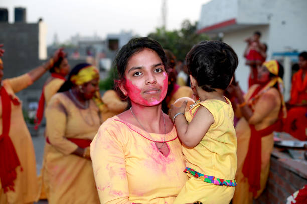 Mother and baby girl celebrating Holi festival at home on rooftop. Hindu festival, originating from the Indian subcontinent. It is celebrated predominantly in India and Nepal. Holi is popularly known as the Indian \
