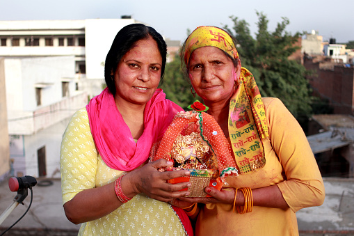 Two Indian rural mature women celebrating birthday of Bal Krishna (Lord Krishna) and portrait with Laddu Gopal.