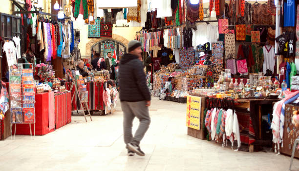 Local man walks through Jarash Souk, near Amman, Jordan, Middle East. Busy Souk at the entrance to Jarash ruins, full of clothing, products and souvenirs. Jerash is the modern name of the remarkably well=preserved ancient city of Gerasa in Jordan, north of Amman. Inhabited since the Bronze Age, the ruins of the walled Greco-Roman settlement outside the modern city are more extensive than either Rome or Pompei. having been protected by and buried in sand for centuries. Featuring the 2nd-century Hadrian’s Arch, Corinthian columns of the Temple of Artemis and the huge Forum’s oval colonnade that leads to the Cado main thoroughfare
