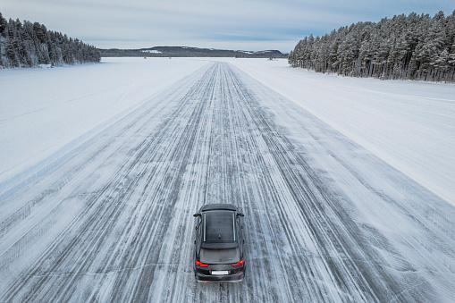 High angle view of a car travelling the slippery road of an icy lake in the snowy landscape, Skabram lake, Jokkmokk, Swedish Lapland, Sweden