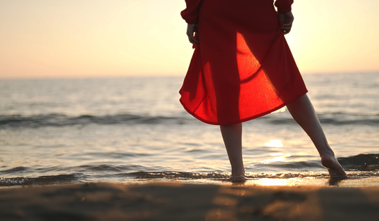 Woman in red stands in the sea at sunset.