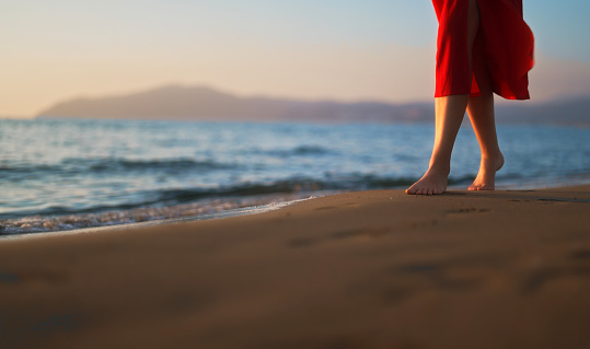 Woman in red dress walks along the beach.