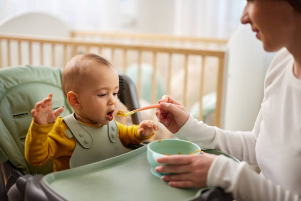 istock Mother spoon feeding her baby son at home 1470461379