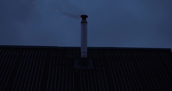 Smoke and sparks fly out of the chimney onto the roofs of the house. Kindling the stove in the baths. Against the background of the sky, smoke is coming from the chimney on the roof of the bathhouse..