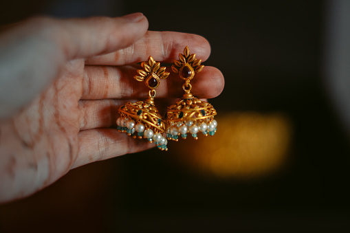 Gold Indian women's earrings in hand. Gold wedding Jewelry of Indian bride. Beautiful Jumaka earrings.