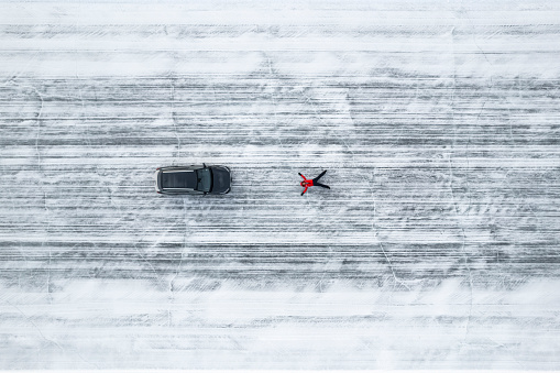 Top view of a tourist lying on an icy road above a frozen lake near a car