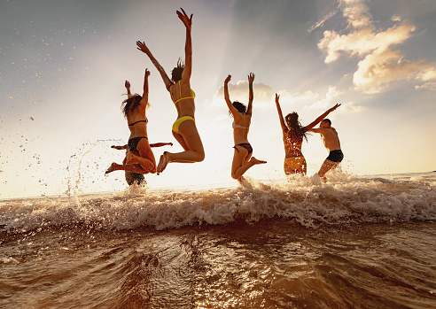 Group of happy young friends are having fun and jumps at sunset sea beach