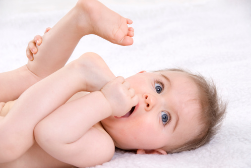 cute baby lie down on white fur blanket and hold foot putting into  mouth in studio white background