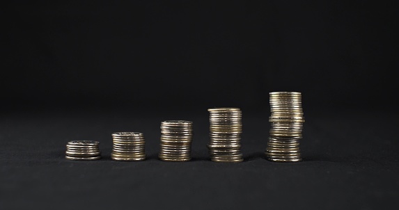 Five stacks of coins stand in a row on a black background. Stacks of coins stand on a black background in ascending order. The concept of increasing financial income..
