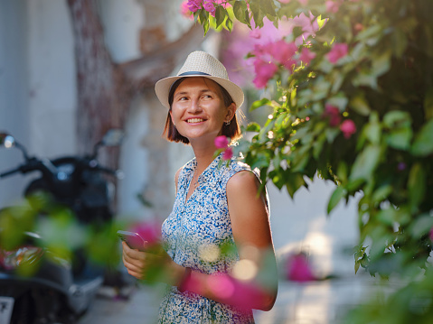 Blooming bougainvillea, streets of the old town of Bodrum, Turkey. Happy traveler woman in white elegant outfit walking by romantic streets . Summer travelling