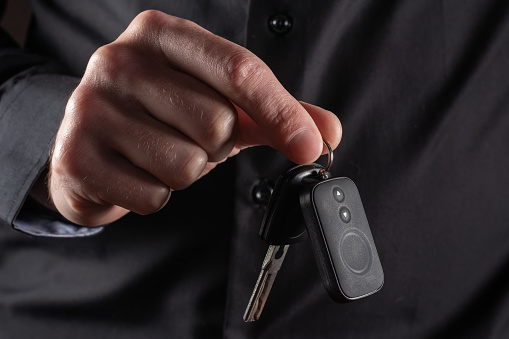 Businessman holding a car key on dark background.
