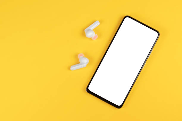 istock Mobile phone with empty screen and earphones on yellow surface. Wireless earphones, mobile phone on yellow background 1470480855