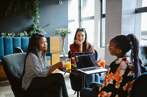 Female colleagues have a team building discussion over work, sitting in a cafe / cantina, talking informally about their IT business.