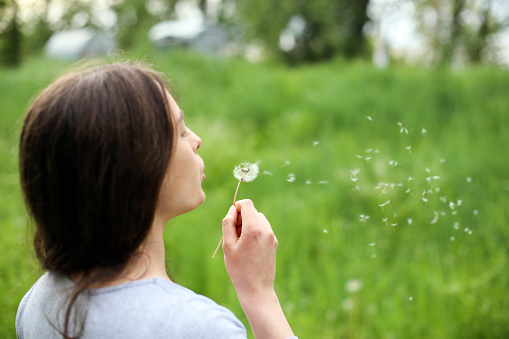 Young woman blowing a dandelion in nature. About 25 years old, Caucasian brunette.