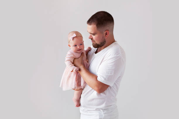 Portrait young Dad holding newborn baby girl in pink dress on white background. Happy father's day. Space for text stock photo