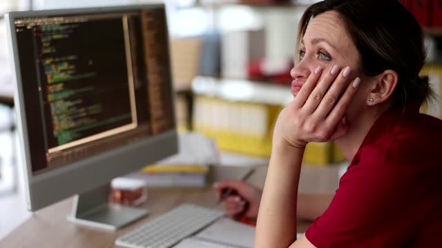 Bored woman sits at computer in office and looks into distance unable to work