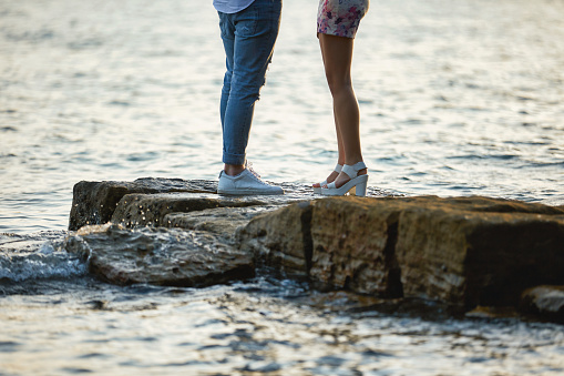 Close-up of legs of a young couple standing on a rock by the sea