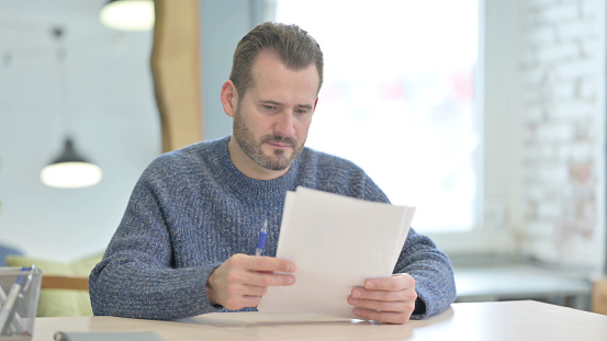 Mature Adult Man Reading Documents in Office, Paperwork