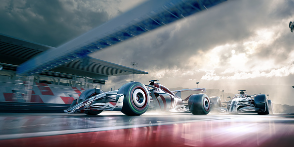 A team of two generic racing cars with a red and metallic livery moving at high speed with wet weather tyres in wet conditions on a generic racetrack past an empty spectator stand. A low angle view with motion blur to the back elements and wheels.