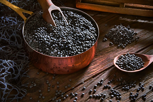 Healthy eating series: Close-up low key image of black lentil in cooper cooking pot 
on rustic wooden table