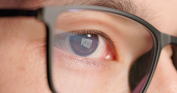 close up view - eyes of asian man is using computer and the shadow from the computer screen reflected on his glasses