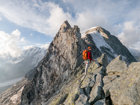 View of skilled climber on mountain crest reaching for the summit. Swiss Alps.