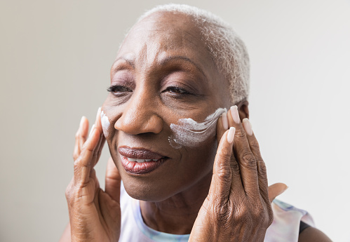 Senior Black woman with grey hair applying moisturizer to her skin