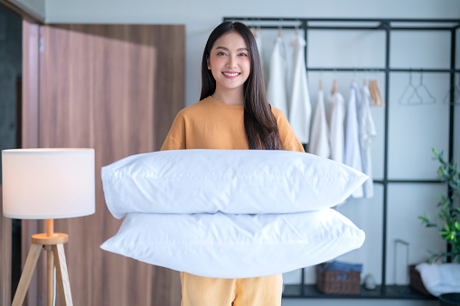 Happy Asian young adult female woman setup her bed sheet blanket by herself in the morning with sunlights from window at home apartment