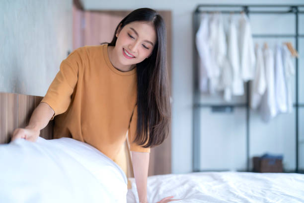 Happy Asian young adult female woman setup her bed sheet blanket by herself in the morning with sunlights from window at home apartment Happy Asian young adult female woman setup her bed sheet blanket by herself in the morning with sunlights from window at home apartment bed sheets stock pictures, royalty-free photos & images