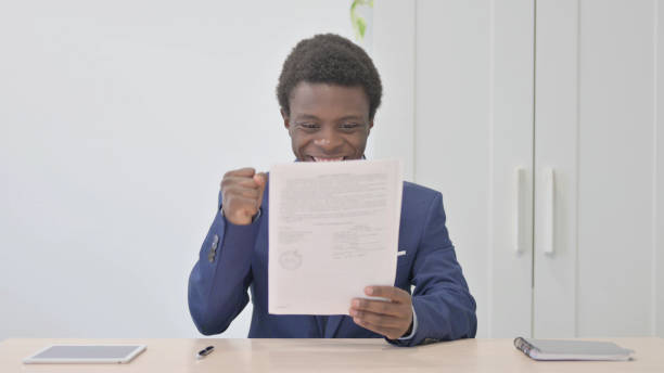 istock Young African Businessman Celebrating Success while Reading Documents in Office 1470502520