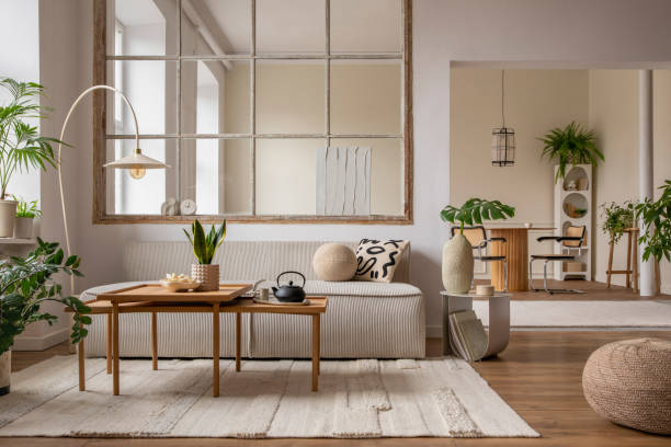 istock Creative composition of living room interior with modular sofa, beige rug, plants, vase with green leaves, pouf, stylish coffee table, big window, lamp and personal accessories. Home decor. Template. 1470504859