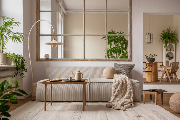 istock Creative composition of living room interior with modular sofa, beige rug, plants, beige pitcher, cup, stylish coffee table, big window, lamp and personal accessories. Home decor. Template. 1470504913