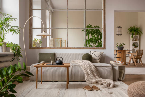 istock Warm and cozy interior with modular sofa, wooden coffee table, big window, patterned pillows, braided plaid, stylish lamp, wooden coffee table, plants and personal accessories. Home decor. Template. 1470504958
