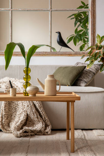 istock Aesthetics composition of open space interior with modular sofa, wooden coffee table, beige pitcher, window, braided plaid, glass vase with leaves and personal accessories. Home decor. Template. 1470504959