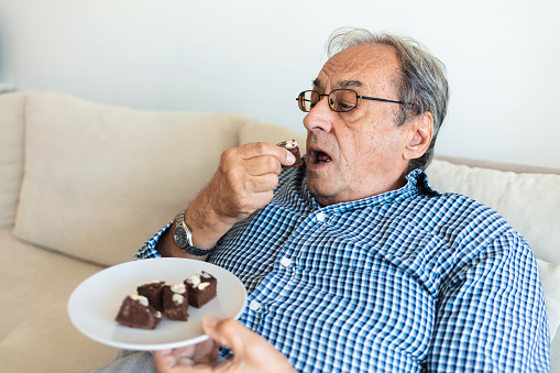 Overweight senior man eating sweet cake. Food addiction, dieting concept. Elderly man eating sweet cake.