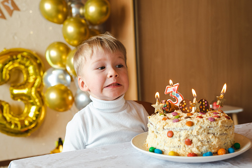 Cute boy making wish on his birthday near birthday cake with candles at home. close-up portrait