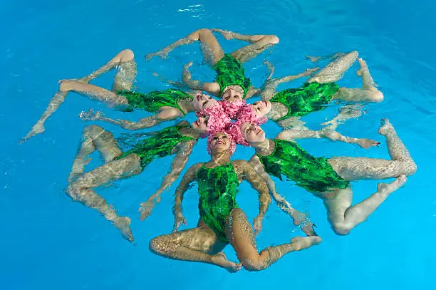 Six synchronized swimmers hold pose for camera. Horizontal format.