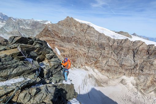 View of skilled climber on mountain crest reaching for the summit. Swiss Alps.
