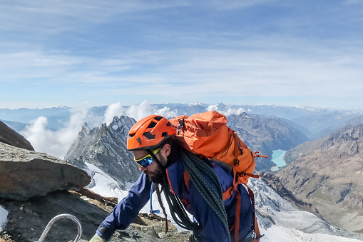 View of skilled climber on mountain crest reaching for the summit. Swiss Alps.