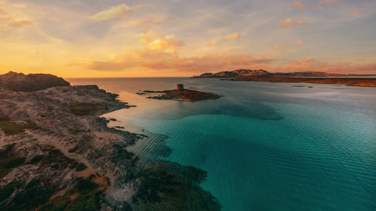 Torre della Pelosa at La Pelosa beach sunset time lapse on the island Sardinia. Mediterranean sea seaside coast of Italy. Yellow and red sky and turquoise water. Cinemagraph seamless video 4K UHD