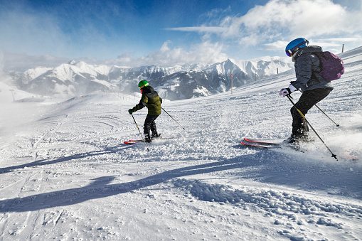Mother and teenage son are skiing together in mountains on a sunny winter day. \nCanon R5