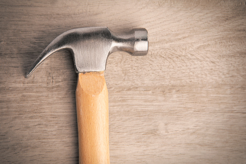 A close up of a hammer head on a wood texture background.
