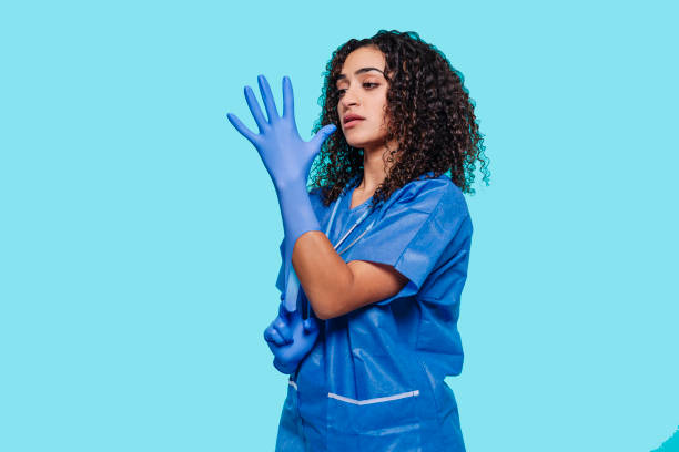 Female nurse putting on blue medical protective sterile gloves Side portrait of young female nurse putting on blue medical protective sterile gloves at hands, isolated over blue background. Health care, medicine, protection, hospital concept. putting on latex gloves stock pictures, royalty-free photos & images