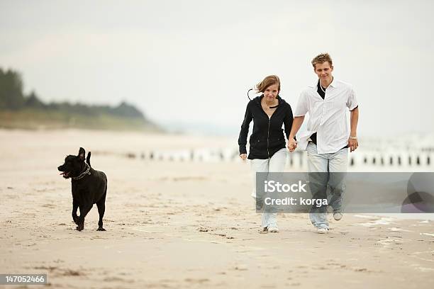 Two Young Poeple Runnig Beach Holding Tight Dog Stock Photo - Download Image Now - Adult, Affectionate, Beach
